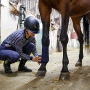 Girl wearing a hard hat bandaging a horse's leg